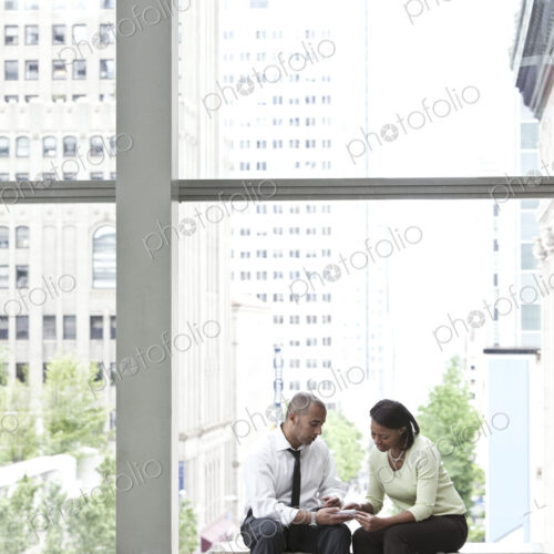 Man and woman seated in an atrium and checking a text on a cell phone. Man and woman seated in an atrium and checking a text on a cell phone.