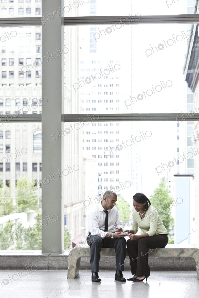 Man and woman seated in an atrium and checking a text on a cell phone.