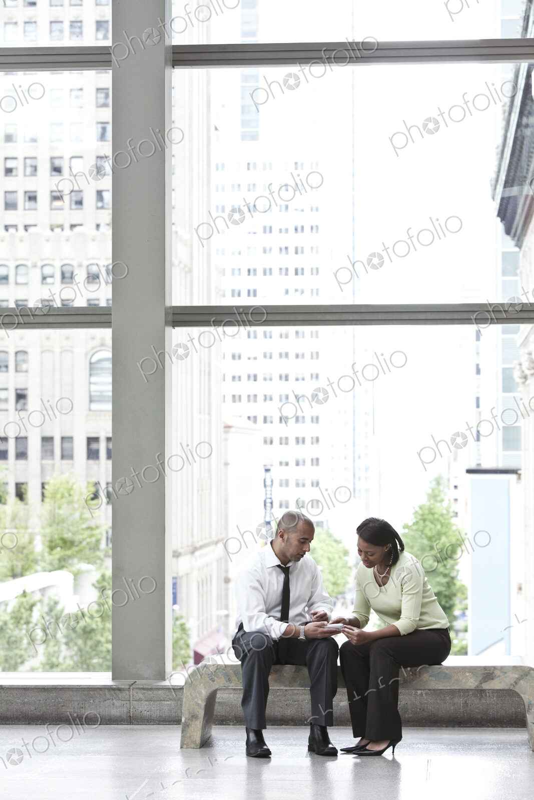 Man and woman seated in an atrium and checking a text on a cell phone.