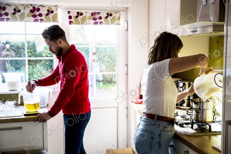 Man and woman standing in a domestic kitchen, making jar candles.