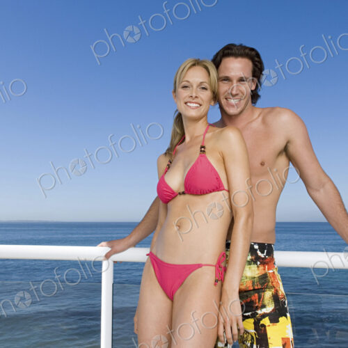 Man and woman standing together at the rail of a cruise ship wearing swimwear.