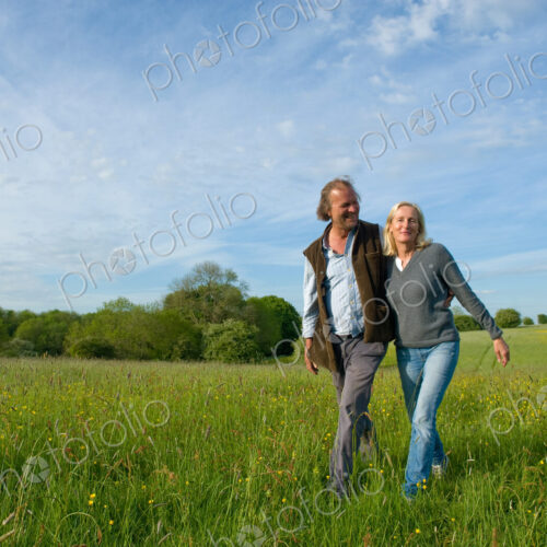 Man and woman walking arm in arm across a meadow.