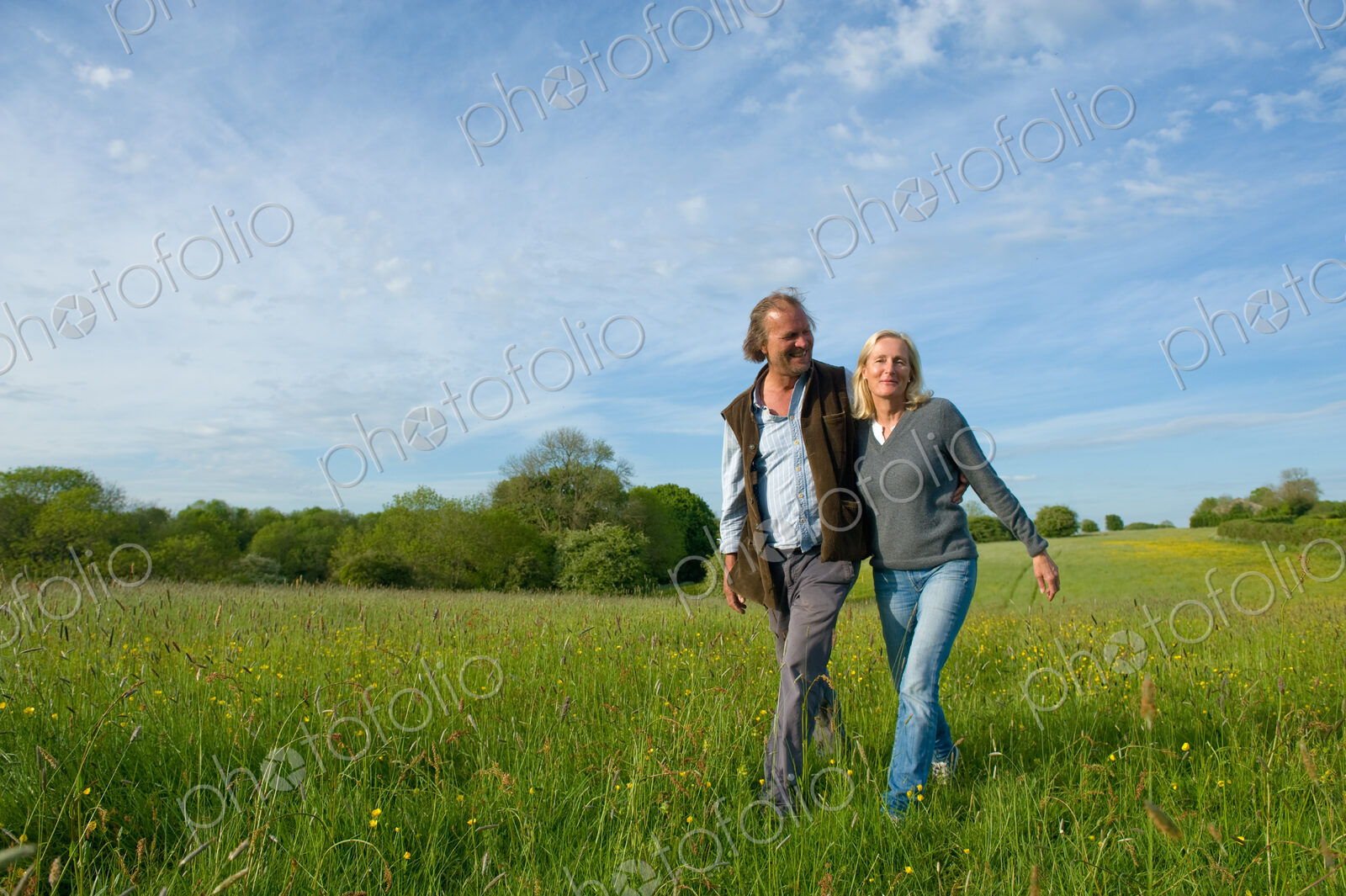 Man and woman walking arm in arm across a meadow.