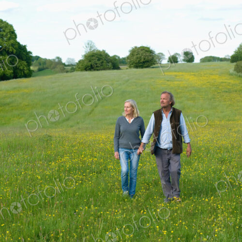 Man and woman walking hand in hand across a meadow.