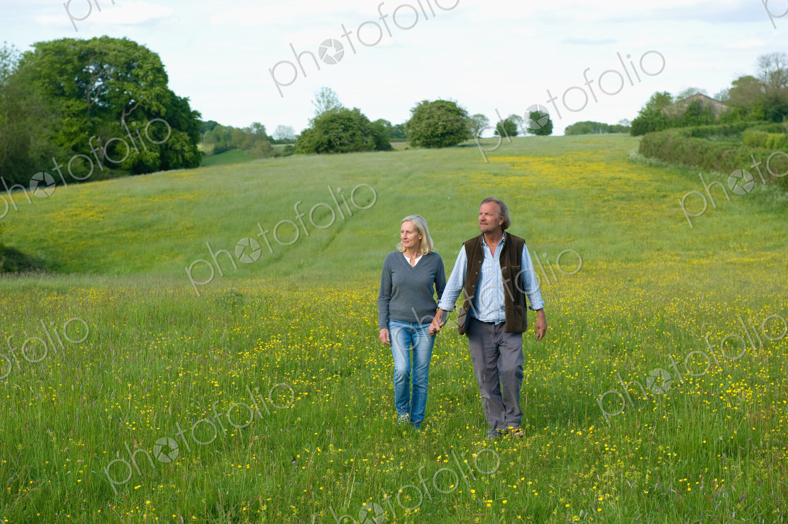 Man and woman walking hand in hand across a meadow.
