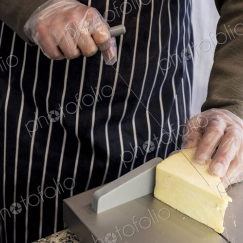Man at counter in a delicatessen, slicing cheese with wire cutter. Man at counter in a delicatessen, slicing cheese with wire cutter.