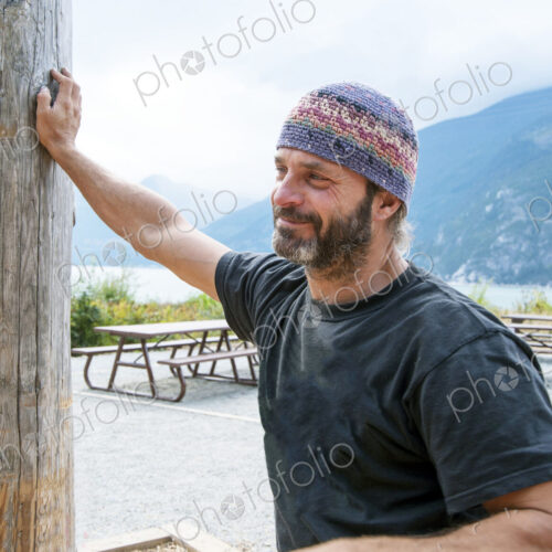 Man at picnic area among mountains wearing knitted hat.