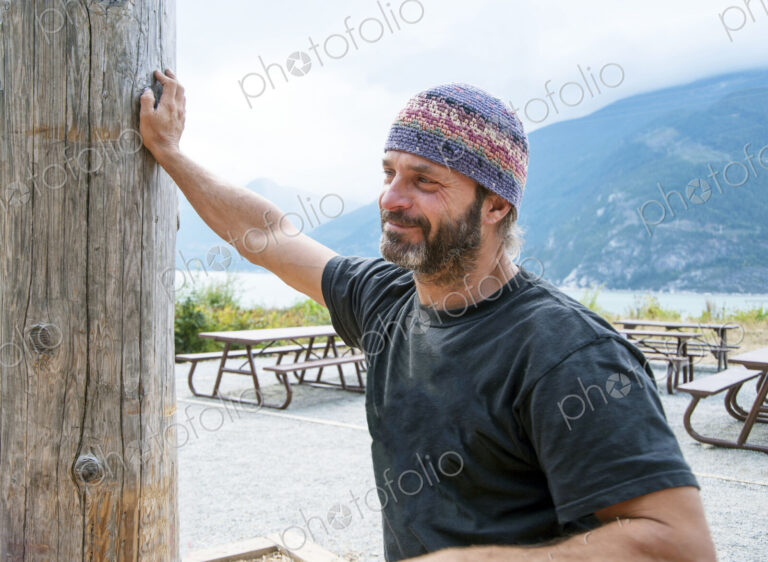 Man at picnic area among mountains wearing knitted hat.