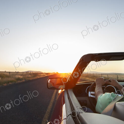 Man at the wheel of his convertible sports car at sunset