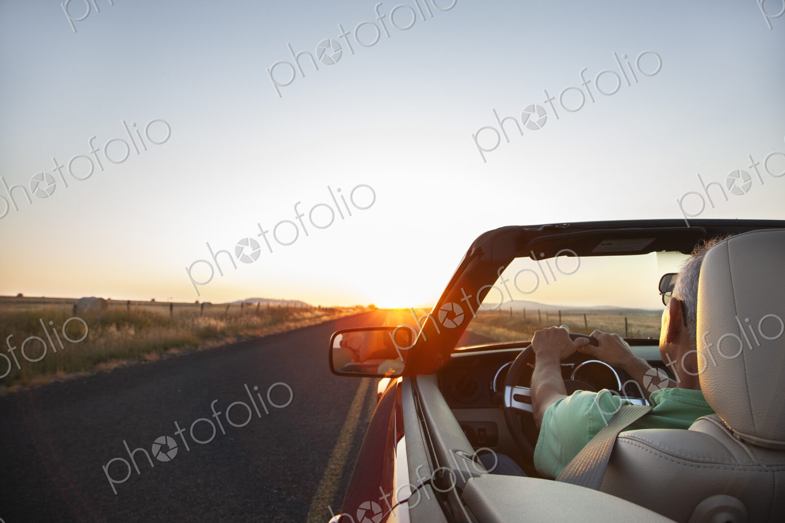 Man at the wheel of his convertible sports car at sunset