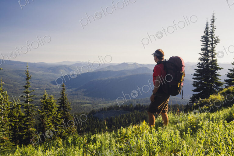 Man backpacking in the mountains, walking on a ridge overlooking a valley.