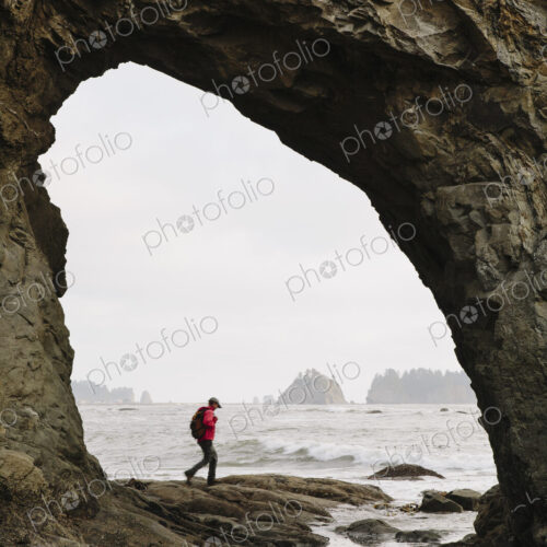 Man hiking on the beach at Hole-in-the-Rock on Rialto Beach Man hiking on the beach at Hole-in-the-Rock on Rialto Beach