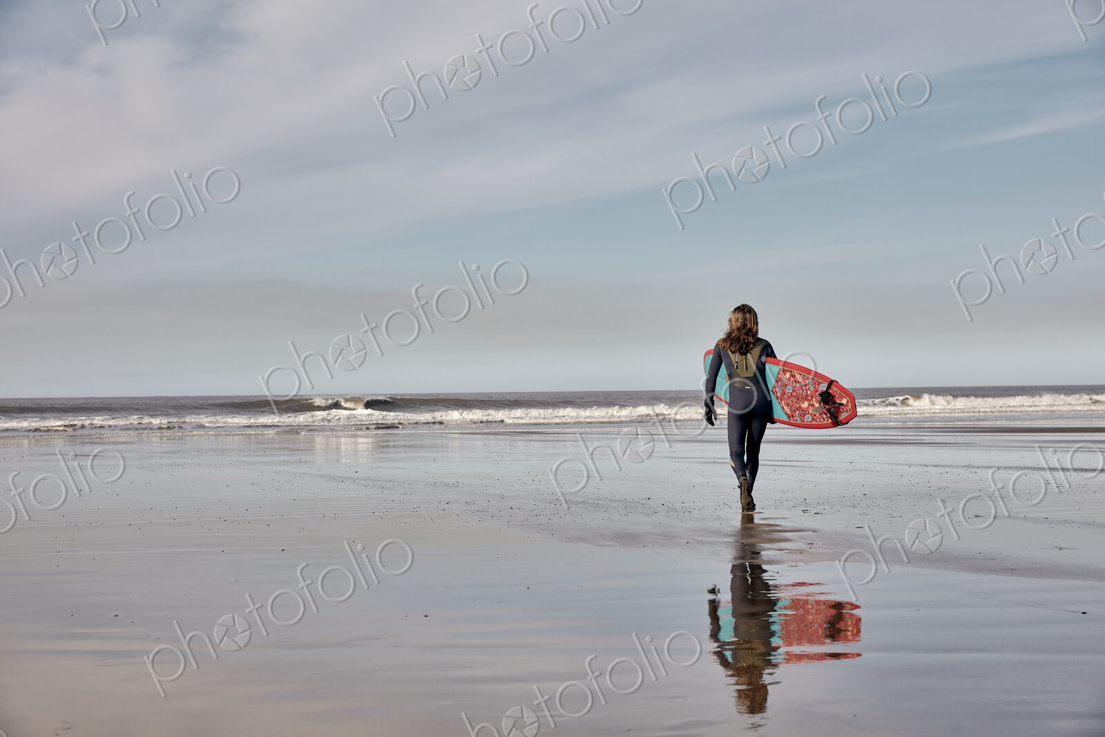 Man holding a surf board walking out to the sea at low tide.