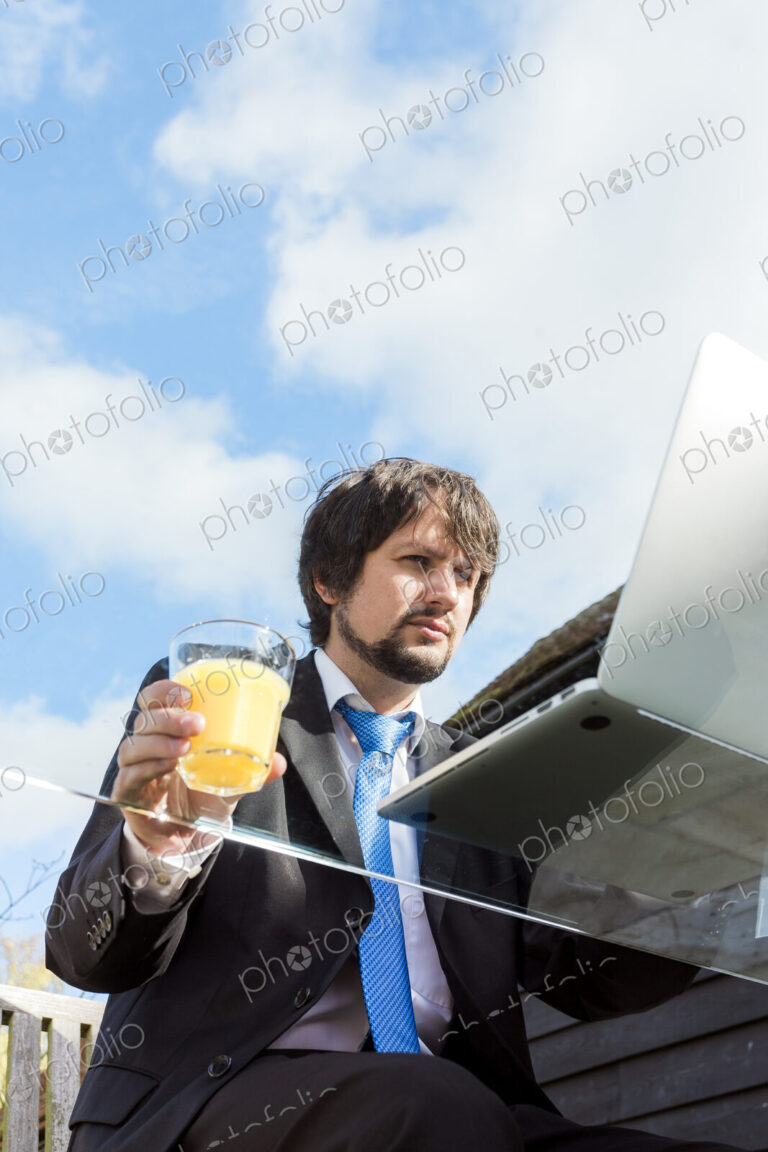 Man holding glass of juice working on a glass desk outside.