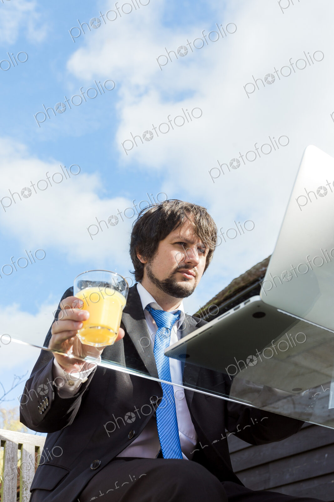 Man holding glass of juice working on a glass desk outside.