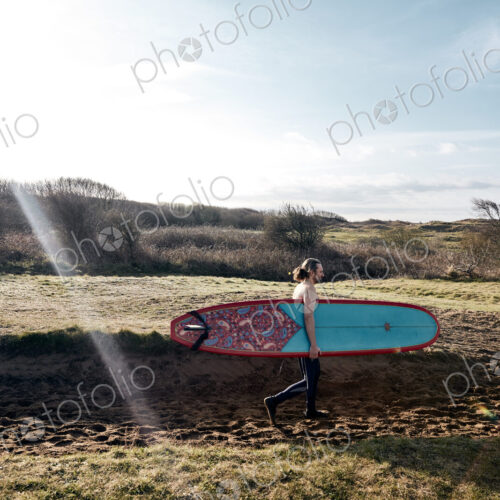 Man holding surf board walking along sandy path towards the sea Man holding surf board walking along sandy path towards the sea