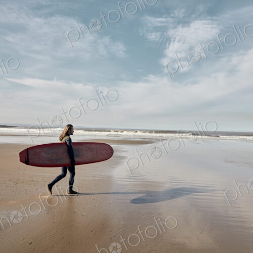 Man in a wetsuit walking towards sea holding a surf board Man in a wetsuit walking towards sea holding a surf board