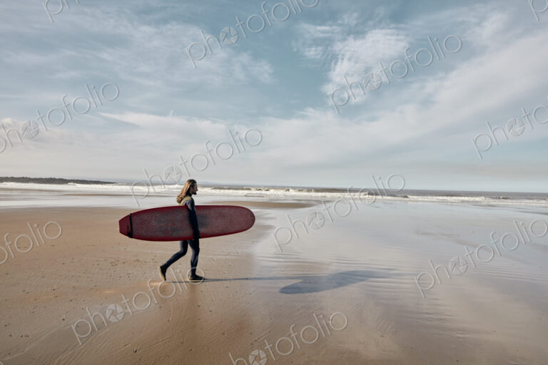 Man in a wetsuit walking towards sea holding a surf board