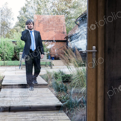 Man in suit walking on path to house talking on a mobile phone. Man in suit walking on path to house talking on a mobile phone.