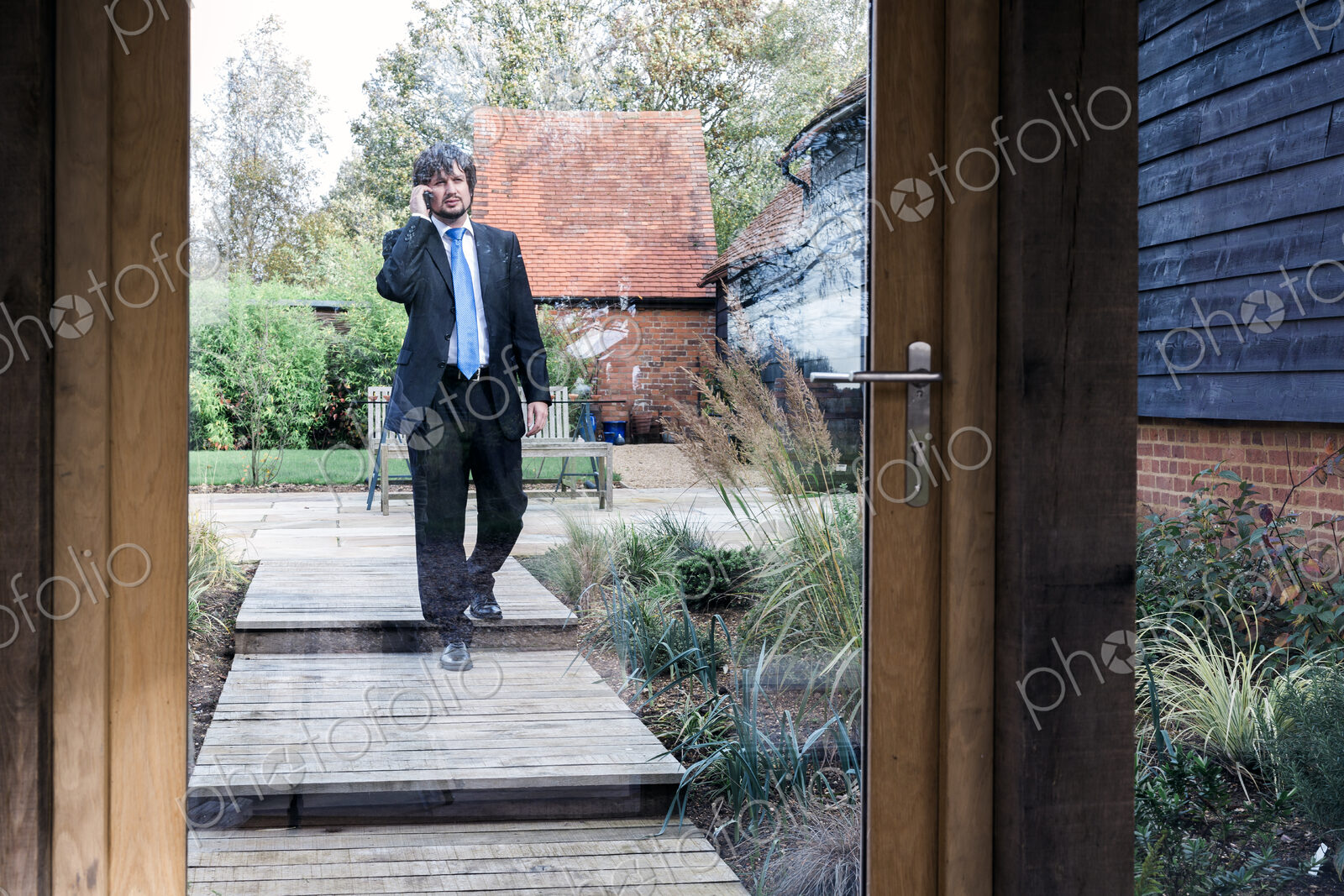 Man in suit walking on path to house talking on a mobile phone.