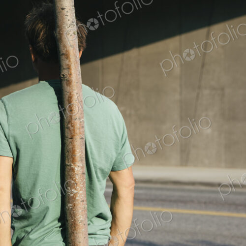 Man leaning against small tree, city street in background