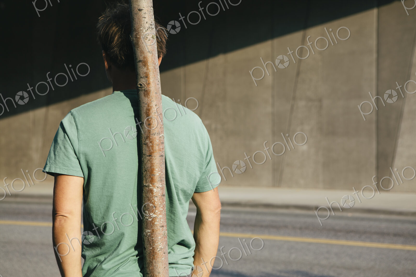 Man leaning against small tree, city street in background