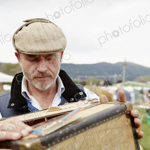 Man looking at a vintage suitcase at a flea market.