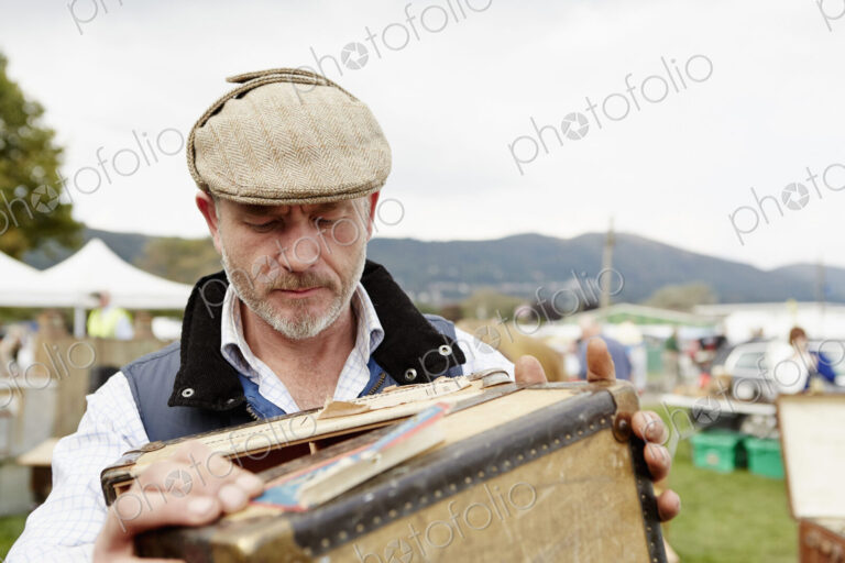Man looking at a vintage suitcase at a flea market.