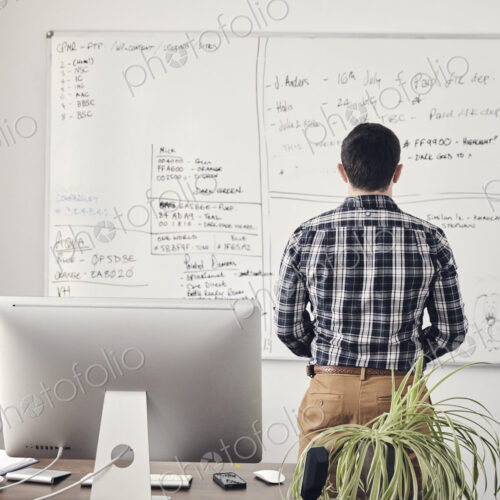 Man looking at a whiteboard in office with his back to camera Man looking at a whiteboard in office with his back to camera