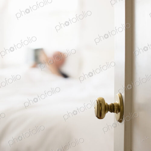 Man lying in a bed with white linen, reading.