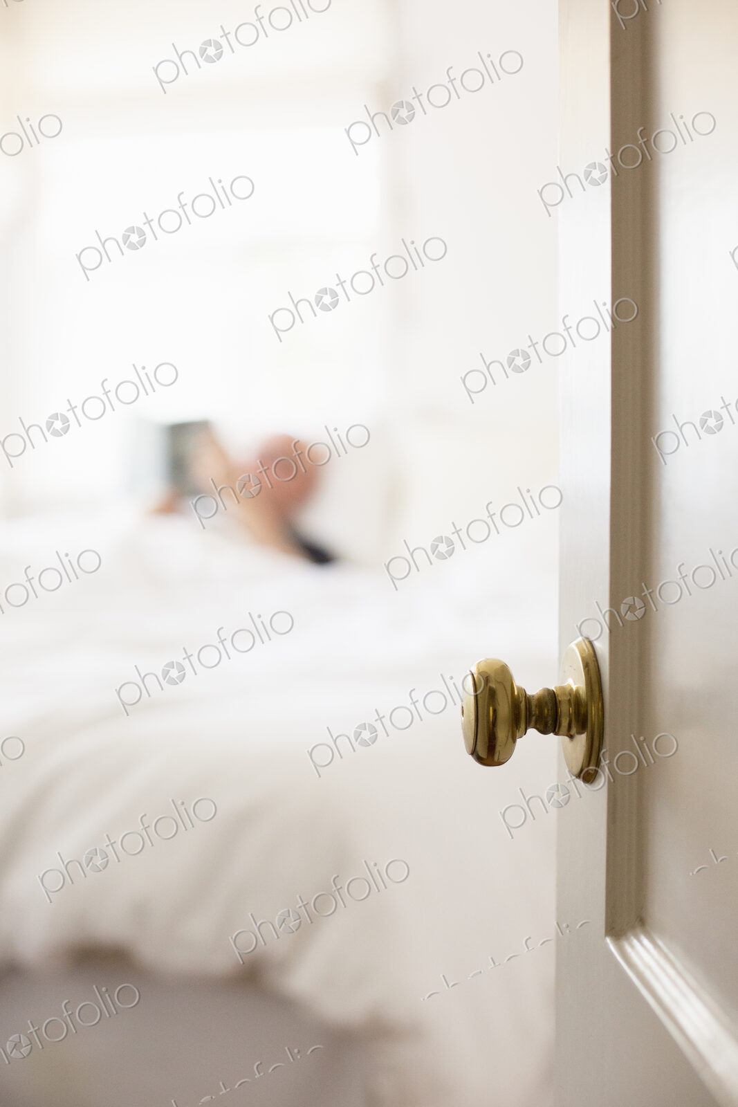 Man lying in a bed with white linen, reading.