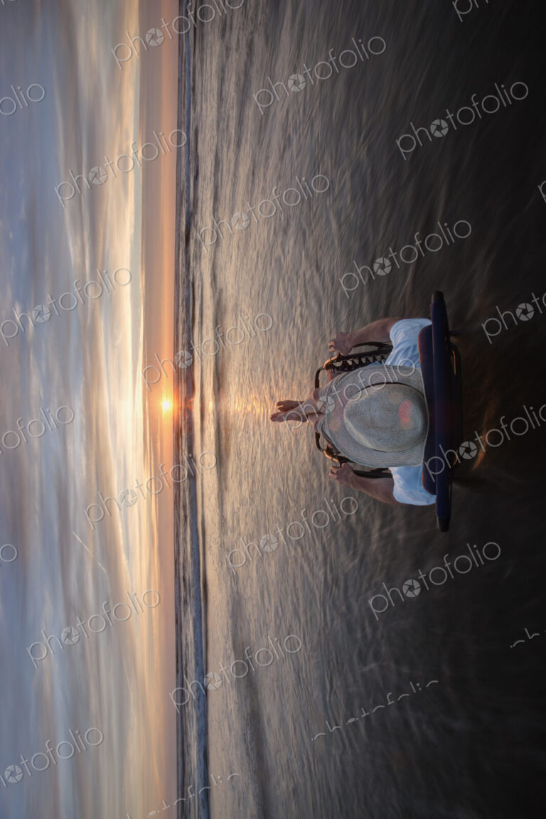 Man lying in sun lounger in shallow wave at beach at sunset.