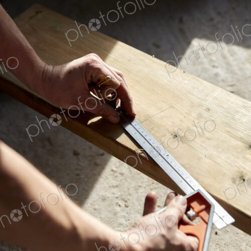 Man measuring a plank of wood using a metal ruler. Man measuring a plank of wood using a metal ruler.