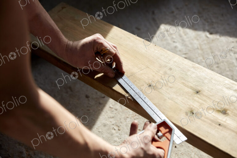 Man measuring a plank of wood using a metal ruler.