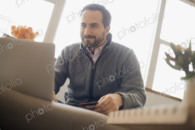 Man on-line shopping on laptop on sofa with credit card