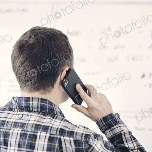 Man on mobile phone with his back to the camera looking at a whiteboard in an office. Man on mobile phone with his back to the camera looking at a whiteboard in an office.