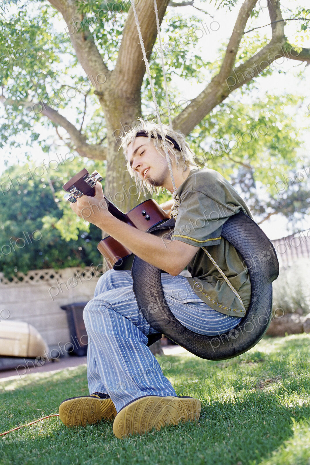 Man playing guitar sitting on a tyre swing in a garden, singing.