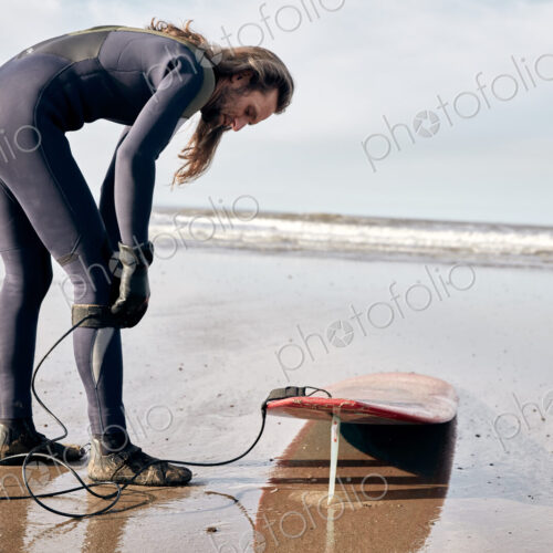 Man preparing to surf on a sandy beach in a wetsuit. Man preparing to surf on a sandy beach in a wetsuit.