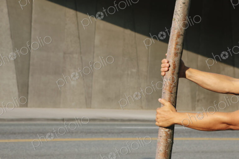 Man pulling on a small tree, on a city sidewalk.