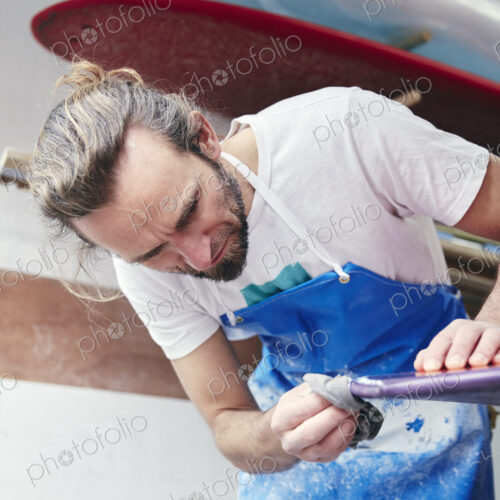 Man sanding and shaping a surfboard in a workshop