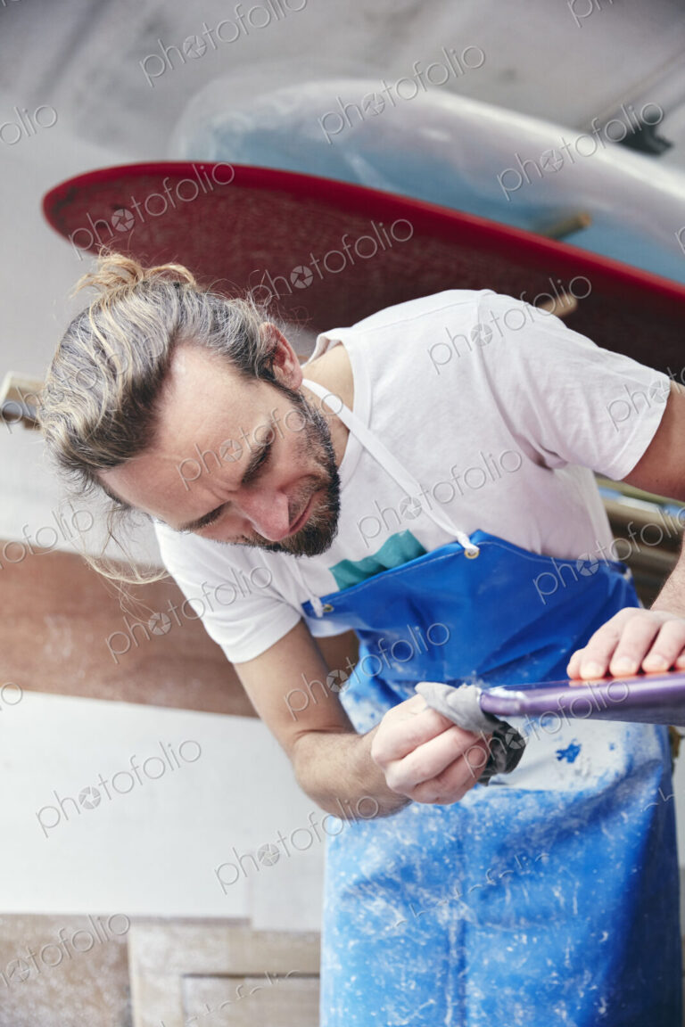 Man sanding and shaping a surfboard in a workshop