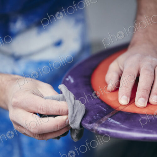 Man sanding and shaping a surfboard in a workshop
