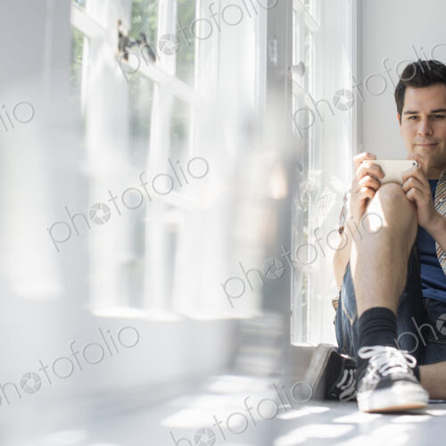 Man sitting by a window, holding a cell phone. Man sitting by a window, holding a cell phone.