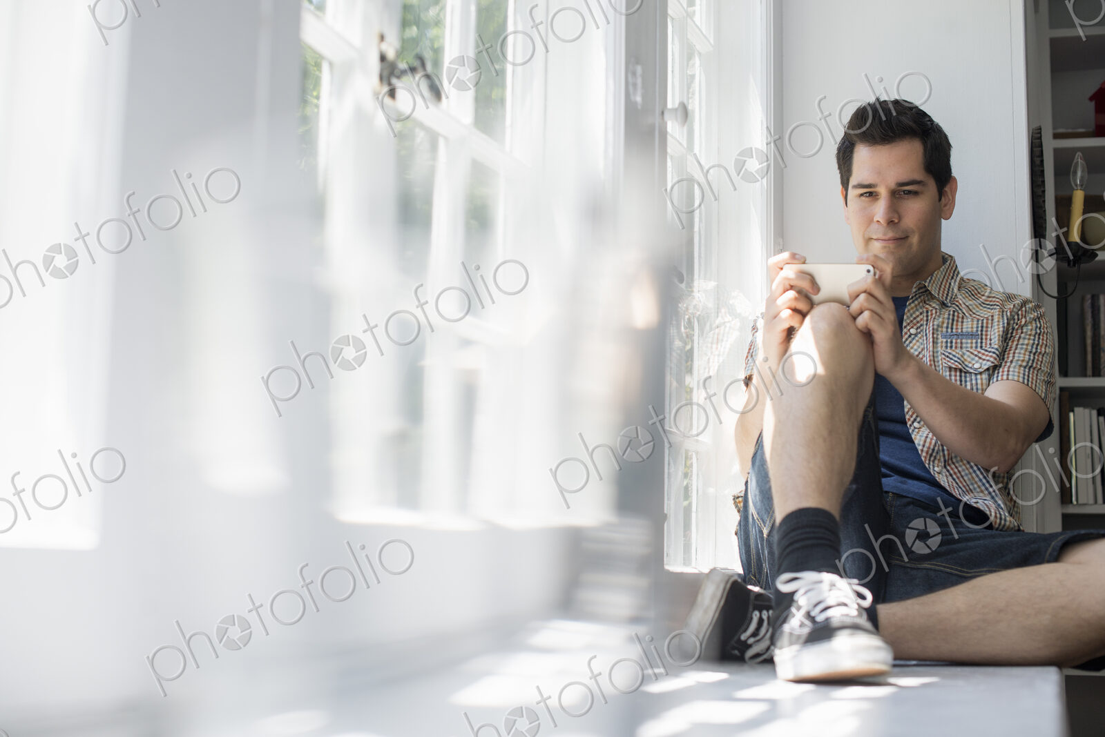 Man sitting by a window, holding a cell phone.