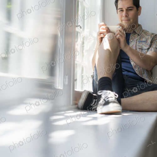 Man sitting by a window, holding a cell phone. Man sitting by a window, holding a cell phone.