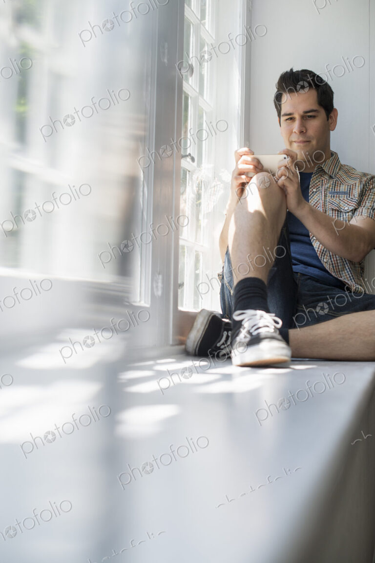 Man sitting by a window, holding a cell phone.