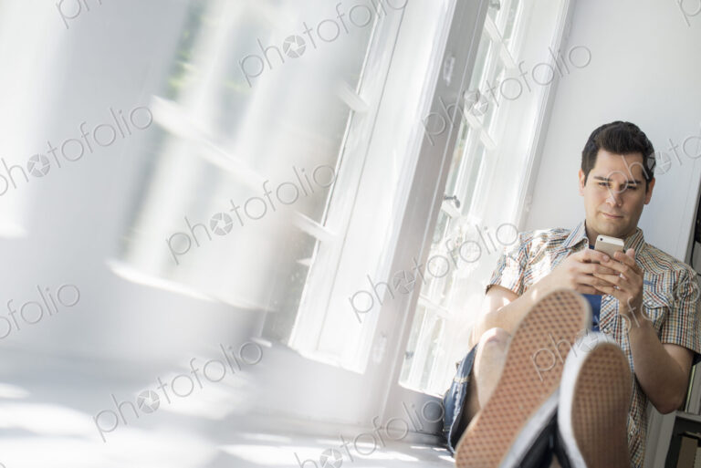 Man sitting by a window, holding a cell phone.