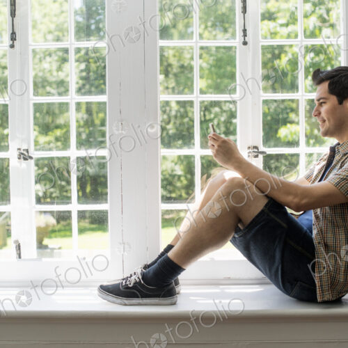 Man sitting by a window, holding a cell phone. Man sitting by a window, holding a cell phone.