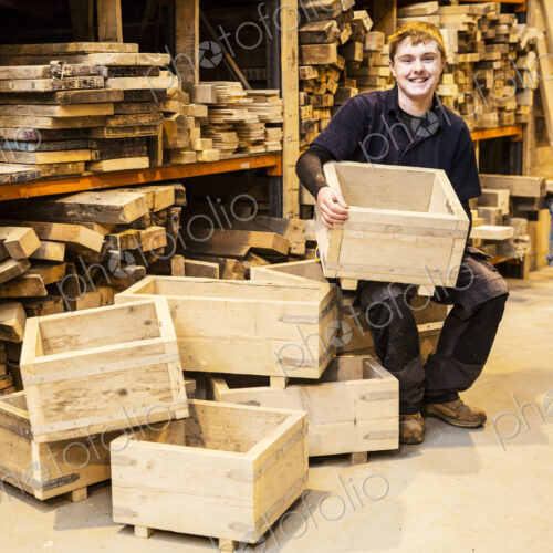 Man sitting in a warehouse in front of shelves with wooden planks, holding wooden…