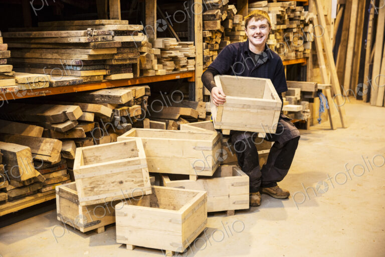 Man sitting in a warehouse in front of shelves with wooden planks, holding wooden…